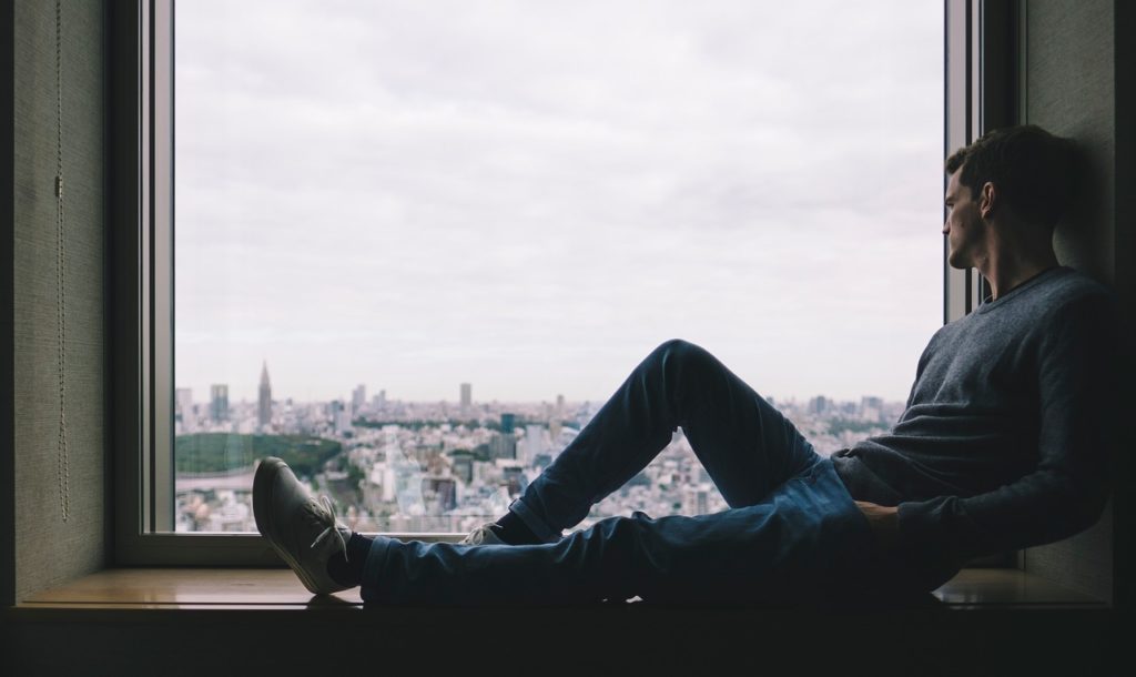 man sitting on window sill overlooking city